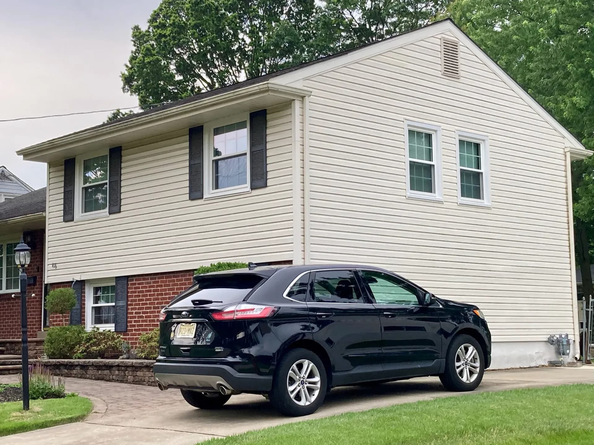 A beige split-level house with brick accents and white trim, surrounded by greenery. A black SUV is parked in the driveway, conveying a suburban feel.
