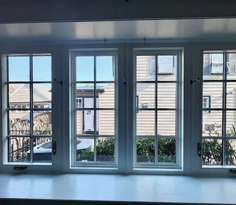 View through three-paneled window revealing quaint, sunlit houses with slanted roofs. Backyard greenery adds a cozy and serene atmosphere.