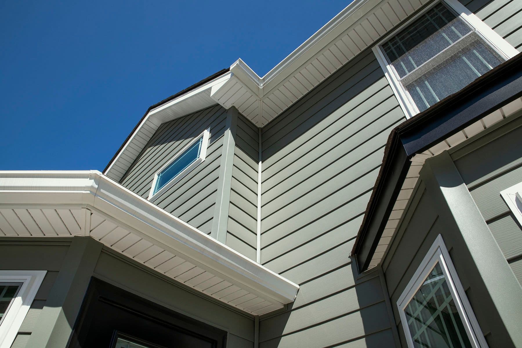 A low-angle view of a modern house with gray siding and white trim against a clear blue sky. The design is sleek and contemporary, conveying elegance.