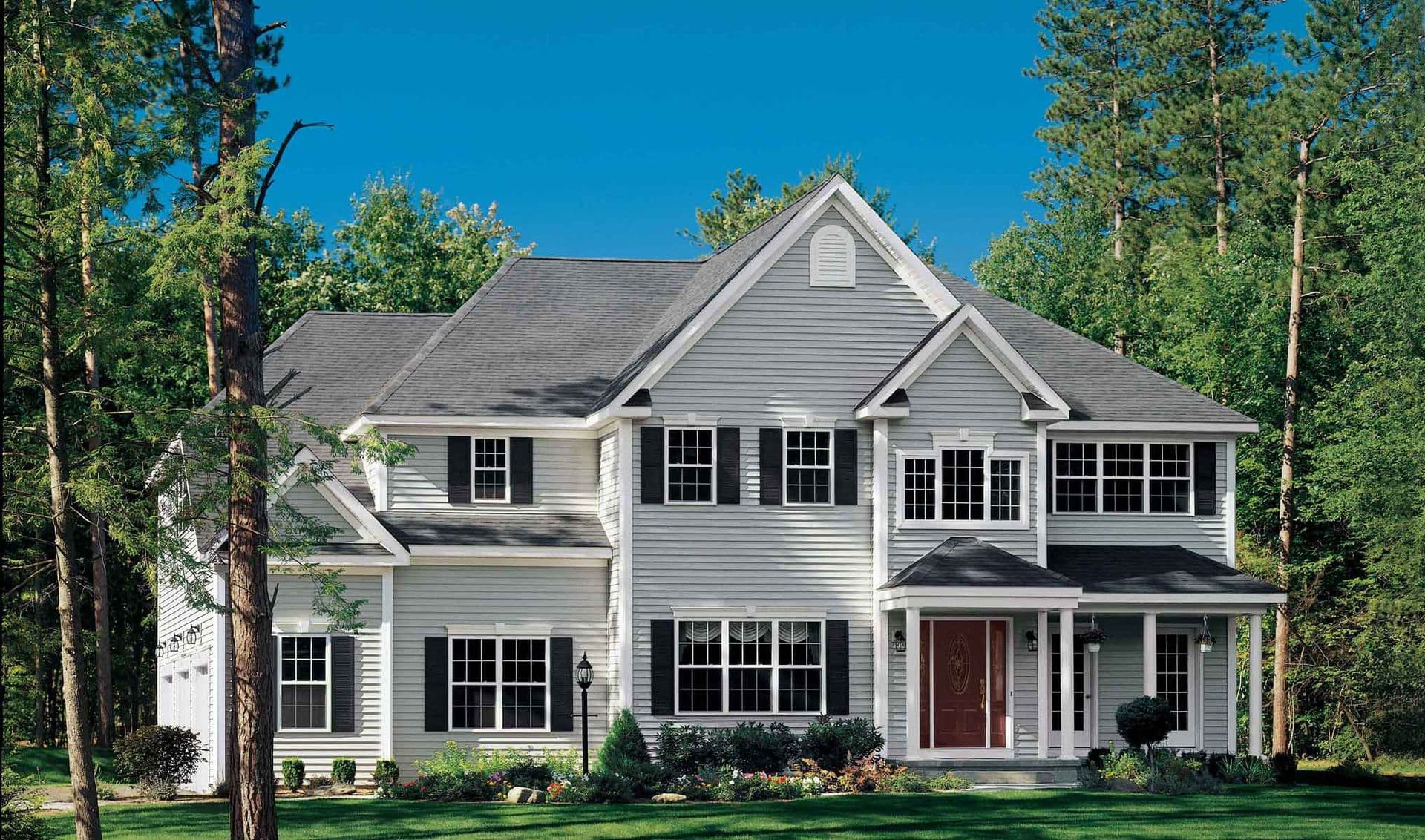 Two-story white house with gray roof, surrounded by lush green trees and grass. Large windows and a welcoming porch create a serene suburban atmosphere.