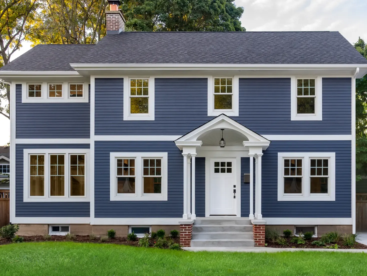 Two-story house with blue siding, white trim, and symmetrical windows. Front porch has columns and a graceful archway. Lush green lawn in front.