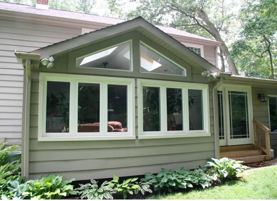A cozy house exterior with a gabled sunroom featuring large windows. Surrounded by greenery, it exudes a tranquil and inviting atmosphere.