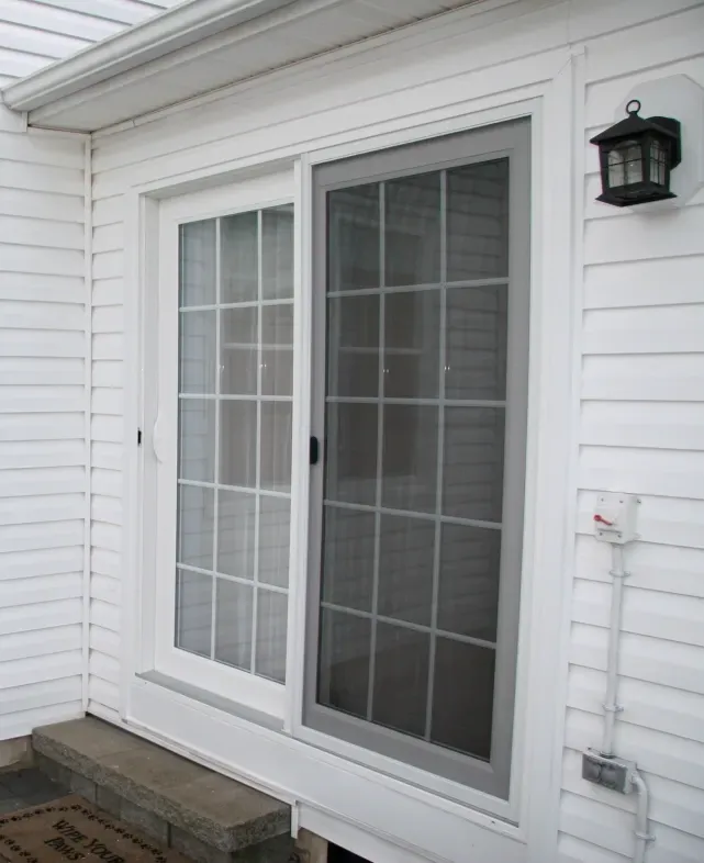 White house exterior with a glass sliding door featuring grid patterns. A black lantern light fixture is mounted beside the door, creating a neat, modern look.