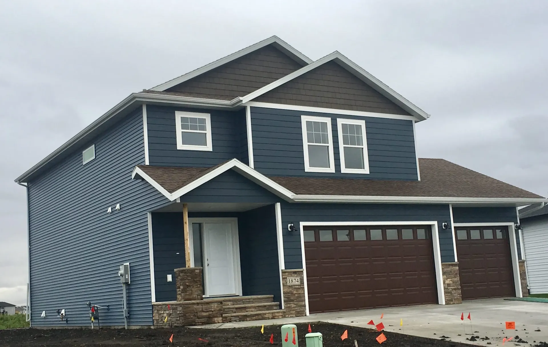 Alt text: A modern two-story house with blue siding and brown accents, featuring large windows and a two-car garage. A cloudy sky looms overhead.