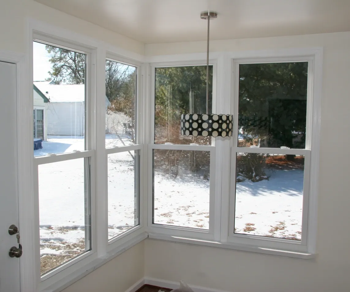 Bright sunroom with large corner windows revealing a snowy yard. A modern pendant lamp with a black and white polka dot shade hangs from the ceiling.