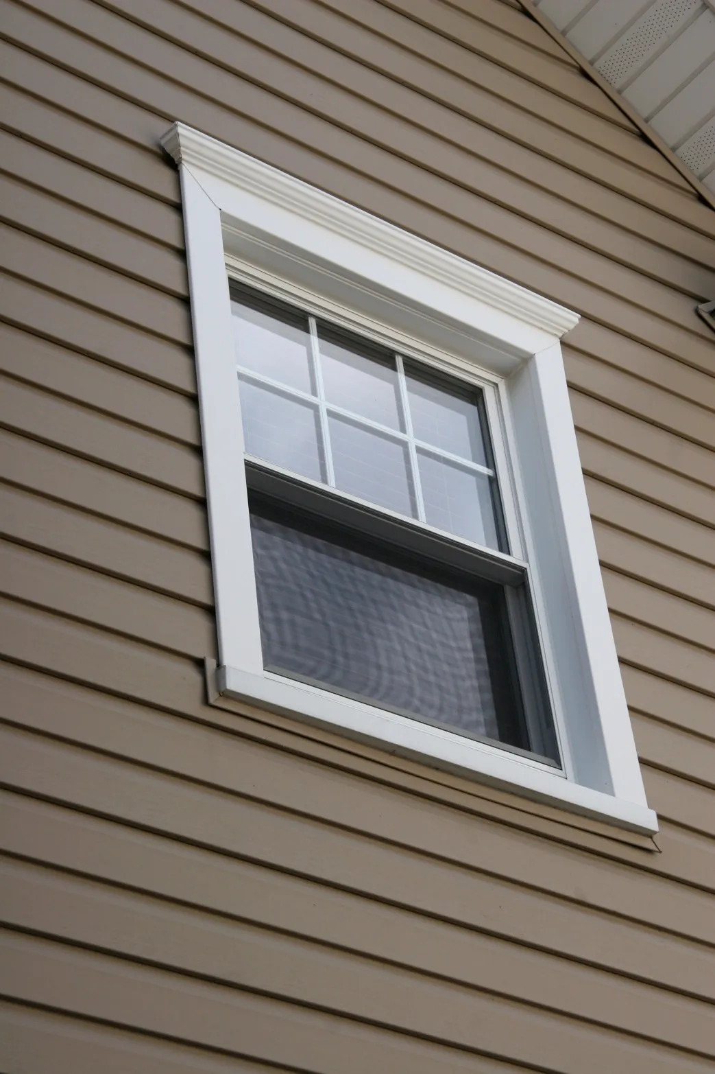A white-framed double-hung window with six panes in its upper sash is set in beige siding. The clean lines create a neat, orderly appearance.